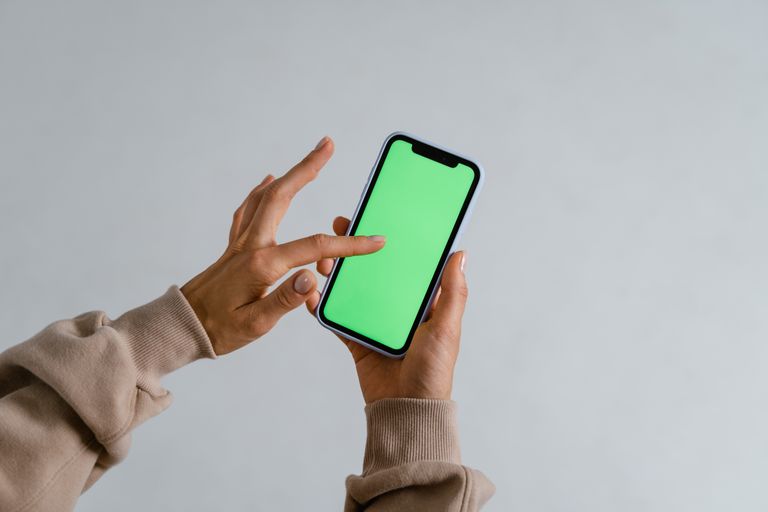 Hands interacting with a smartphone showcasing a vibrant green screen for multimedia use.