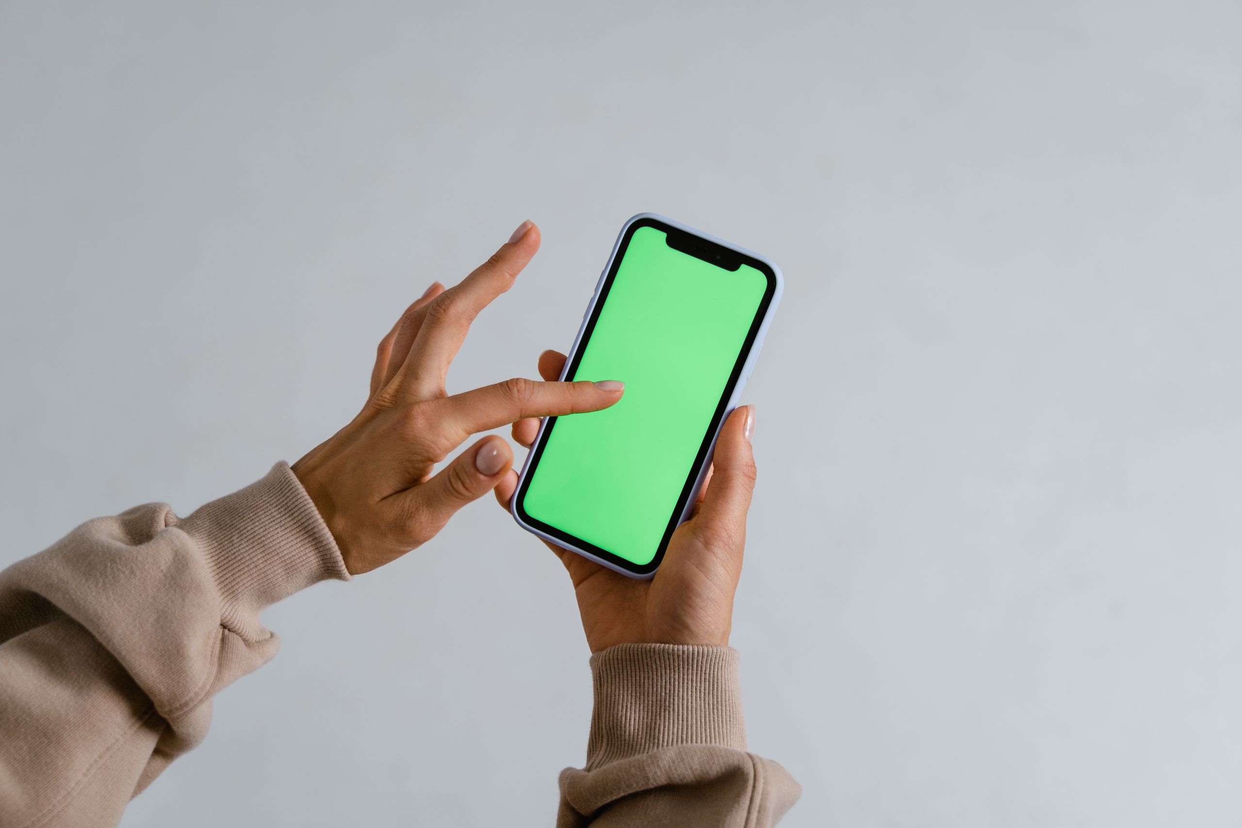 Hands interacting with a smartphone showcasing a vibrant green screen for multimedia use.
